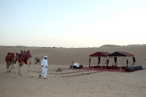 A man leading a camel through the Dubai desert, showcasing the vastness and aridness of the landscape.