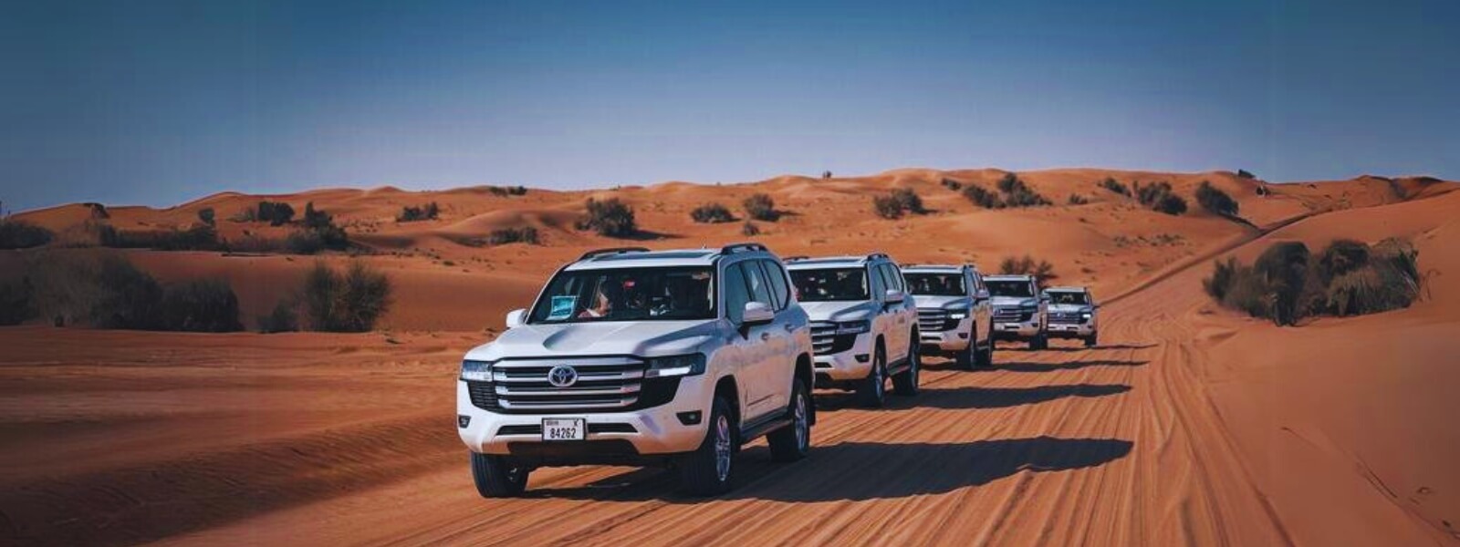 Five vehicles driving down a desert road under a clear blue sky.