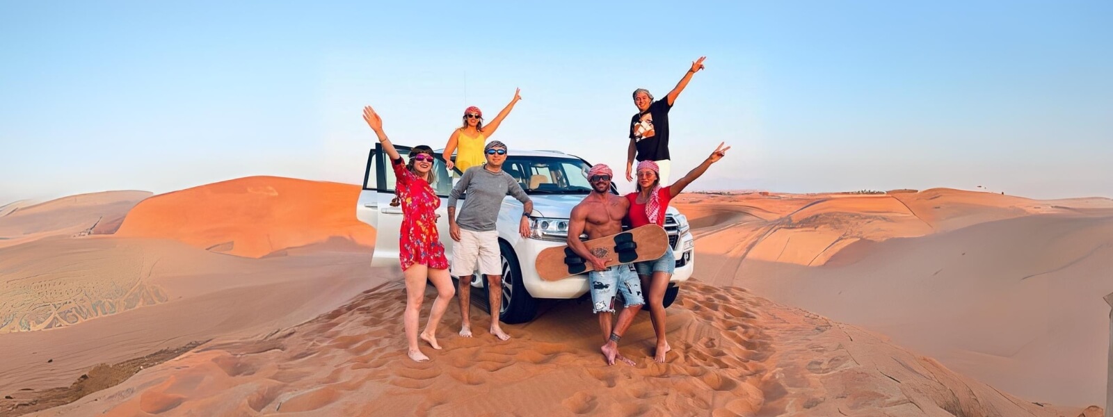 Six people chilling and posing with their vehicle in the desert.