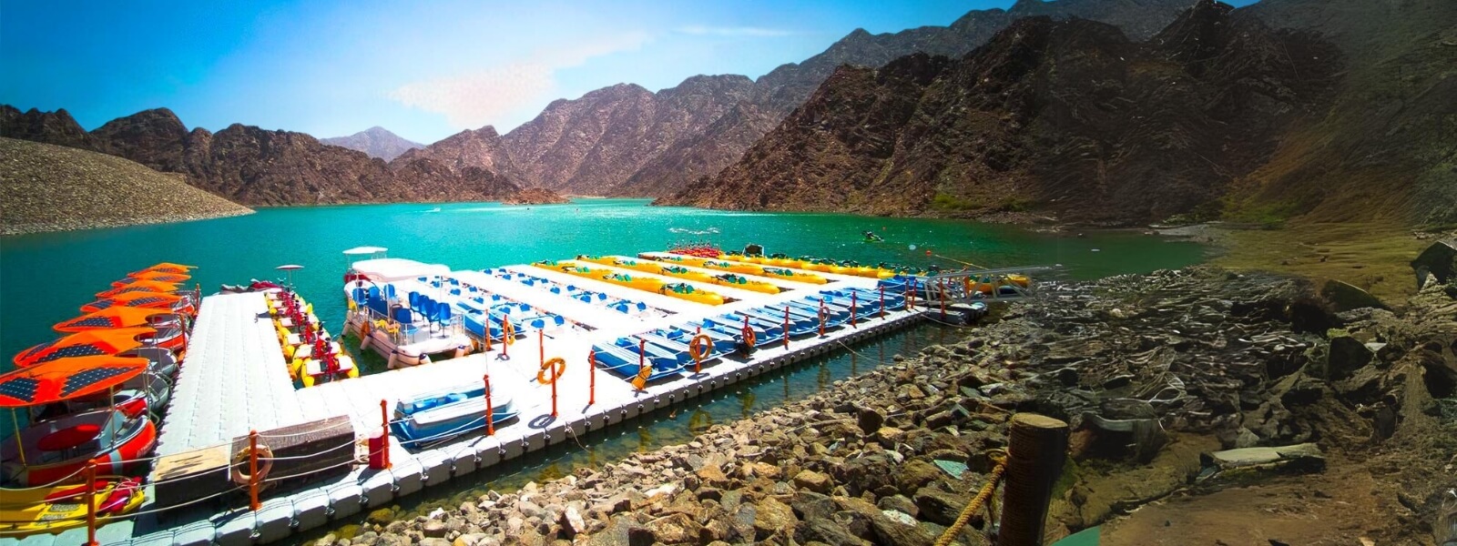 A boat docked on calm water with majestic mountains in the background, showcasing the scenic Hatta sightseeing.