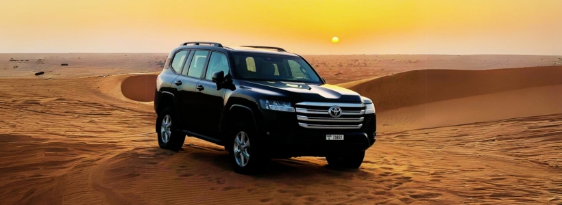 A SUV driving through the desert at sunset, showcasing the vastness and tranquility of the landscape.