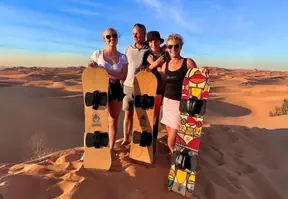 Four people standing with sandboards in the desert, ready for an adventurous day of sandboarding.