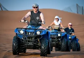 Three people riding ATVs in the desert, kicking up dust as they navigate the sandy terrain.