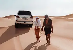 A couple walking in the desert with a car in the background.