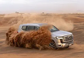 A SUV driving through a desert with sand blowing, creating a hazy atmosphere and a sense of adventure.