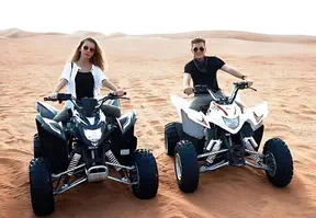 A man and women riding on quad bikes in the desert, enjoying an adventurous and thrilling experience.
