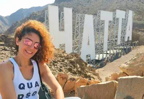 A woman in white top taking a selfie with a landmark features Hatta