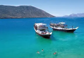 Two boats sailing in crystal blue water with a majestic mountain in the background.