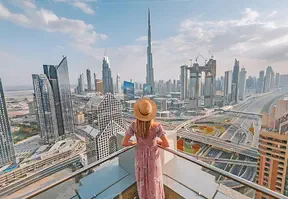 A woman in a pink dress on the balcony overlooking Dubai's cityscape.