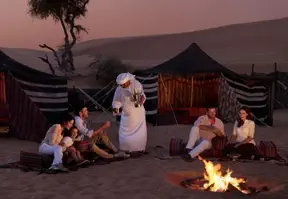 A group of people sitting around a campfire in the desert, under a starry night sky.