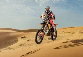 A man on a dirt bike racing through the desert, kicking up dust as he speeds across the arid landscape.