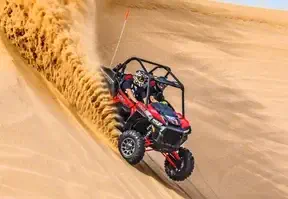 A red buggy through sandy dunes with a person riding a motorcycle on a desert sand dune.