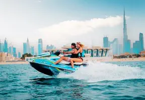 Two people on a jet ski with Dubai skyline in the background.