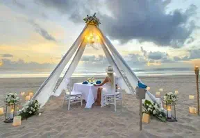A couple enjoying a beachside meal, sitting at a table with the ocean waves and sandy shore in the background.