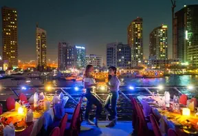 A scenic view of Dubai Marina at night from a dinner cruise boat, with illuminated skyscrapers and a calm waterway.