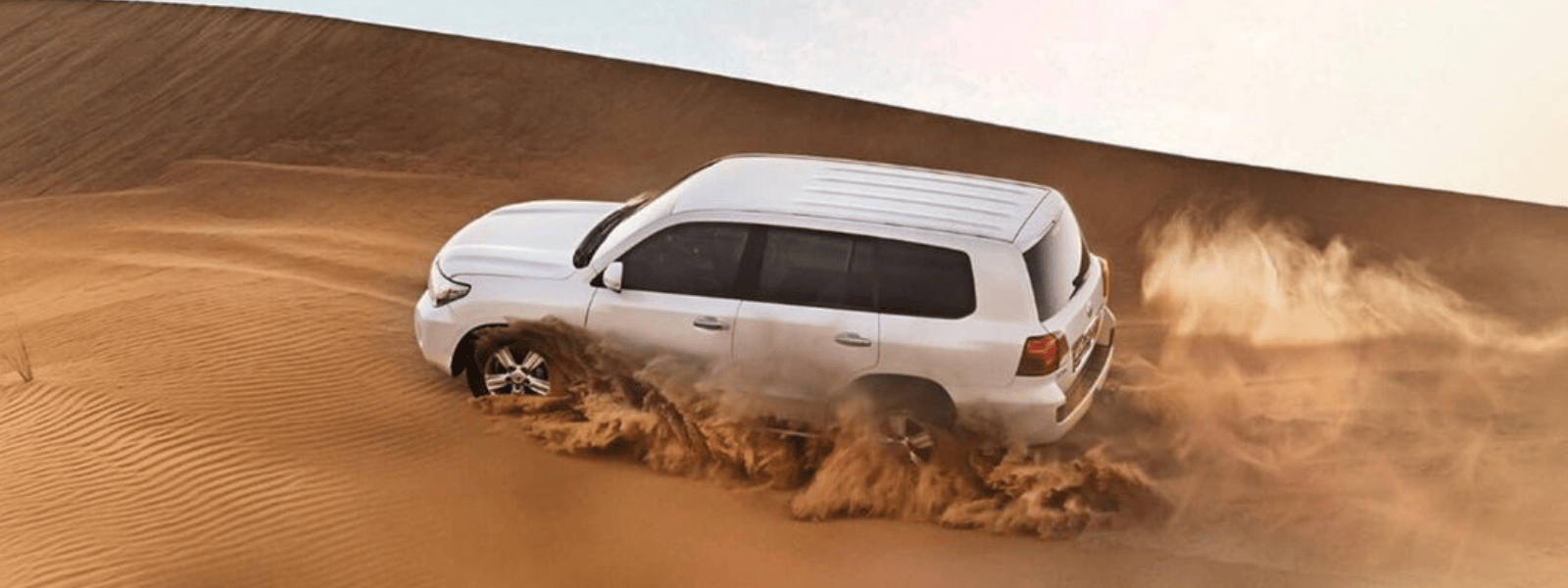 A white SUV maneuvering through sandy dunes, showcasing its off-road capabilities and adventurous spirit.