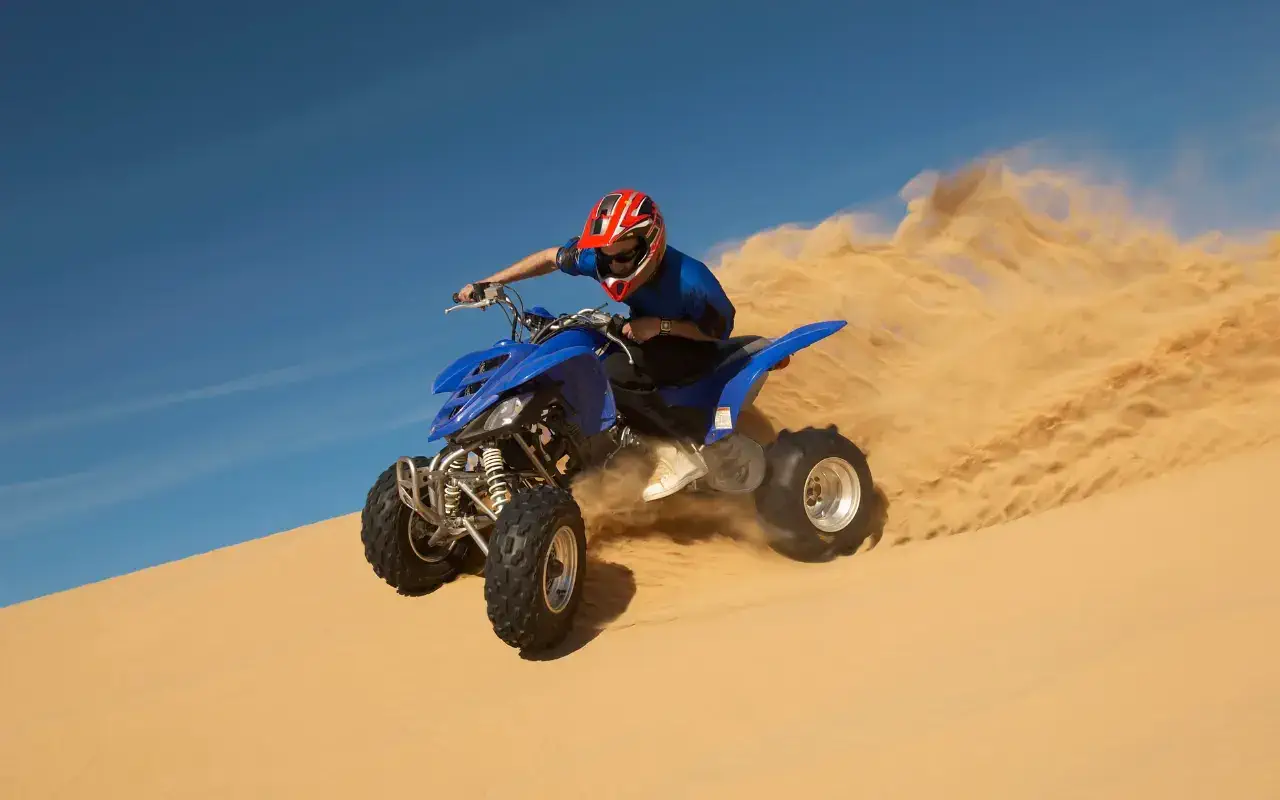 A person riding a blue quad bike on a sandy desert, enjoying an adventurous ride amidst the vast expanse of sand.