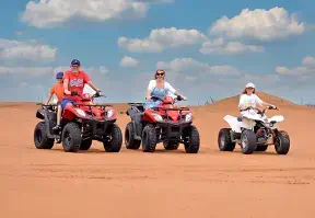 Four people riding three quad bikes in the desert, enjoying an adventurous ride amidst the vast sandy landscape.