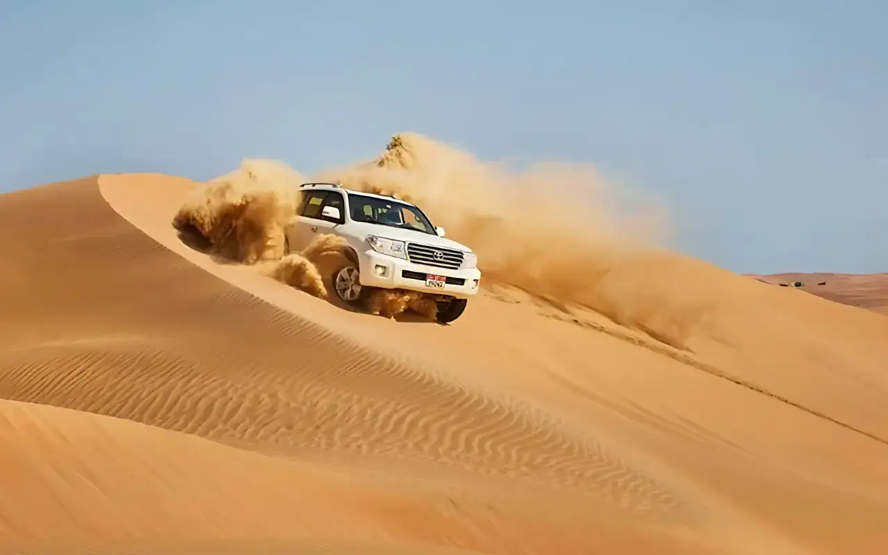 A white SUV driving through sandy dunes, showcasing the vehicle's capability to navigate challenging terrains.