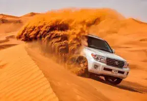 A white SUV driving through a desert with sand blowing, showcasing a rugged adventure in the arid landscape.