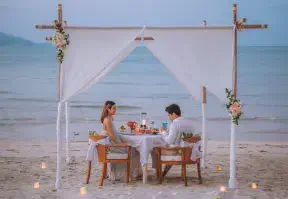 A couple enjoying a beachfront meal, sitting at a table with the ocean in the background.